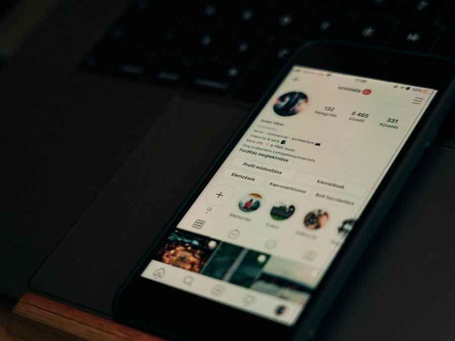 Close-up of smartphone showing a social media profile screen next to a laptop.