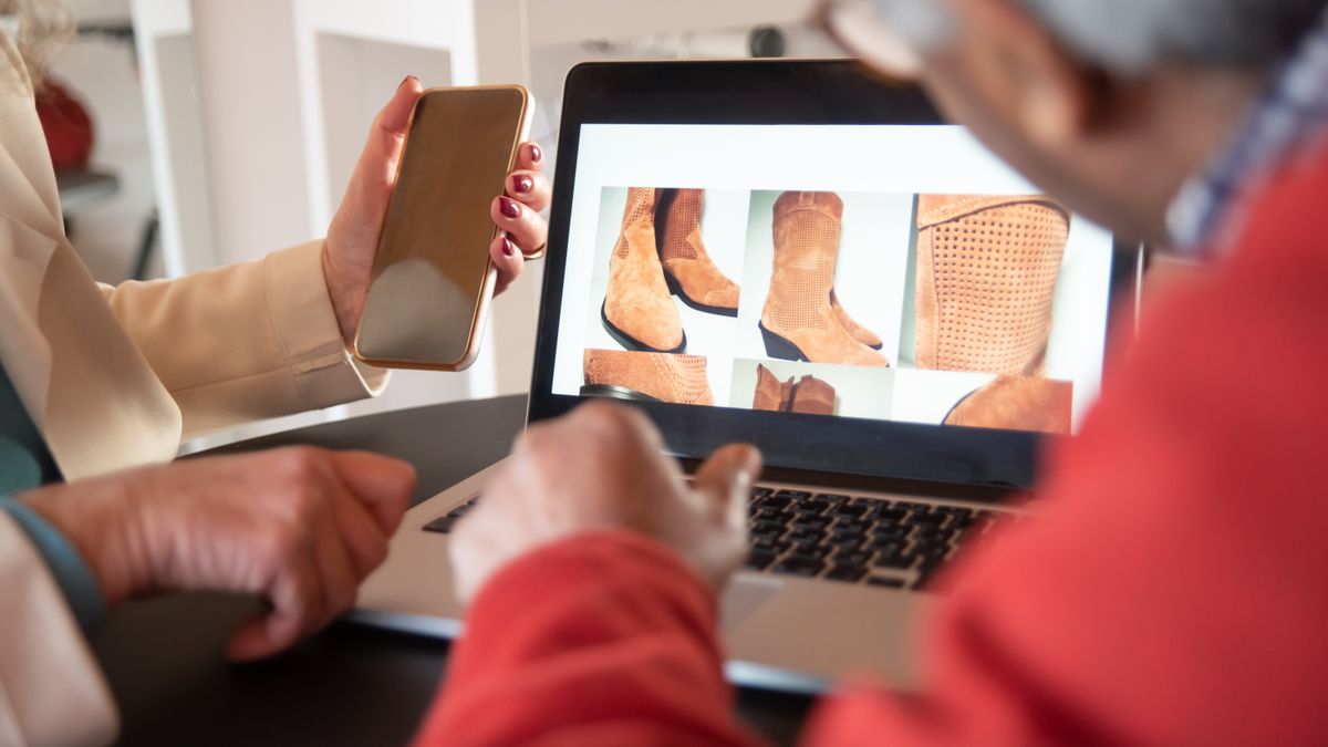 Two people shopping for shoes online using a laptop and smartphone at home.