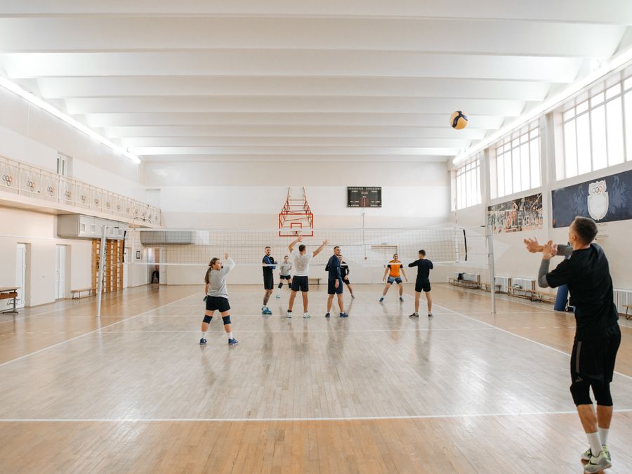 Adults energetically practicing volleyball indoors with a focus on teamwork.