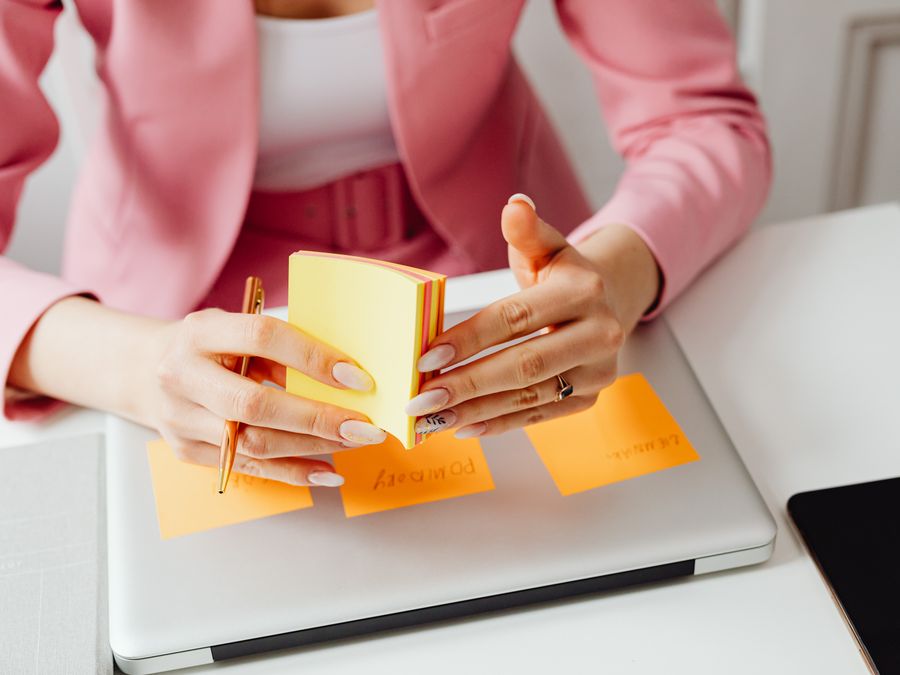 A woman in a pink blazer arranges sticky notes on her laptop, focusing on organization and planning.