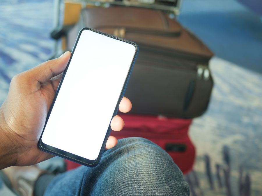 A person holding a smartphone in an airport with luggage visible, ideal for travel and tech concepts.