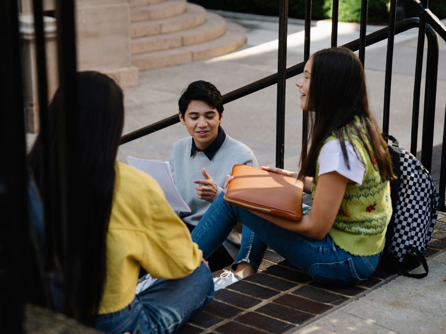 Three college students sitting and talking outdoors on campus.