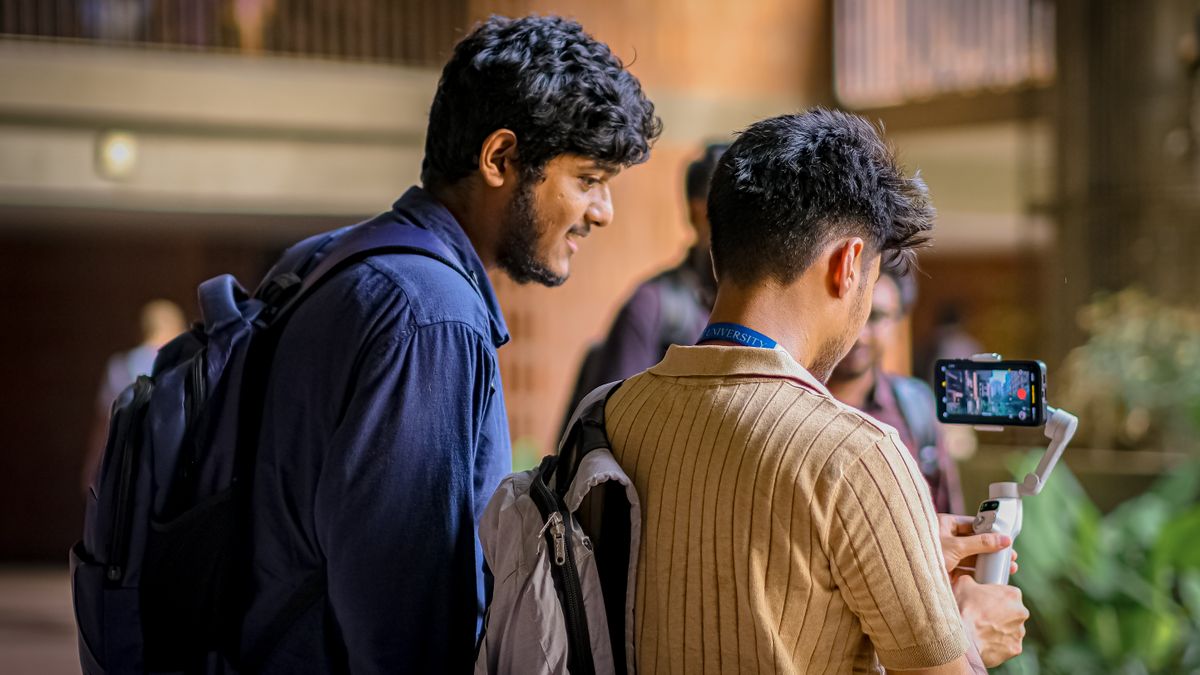 Two students capturing video content using a mobile stabilizer indoors at a university.