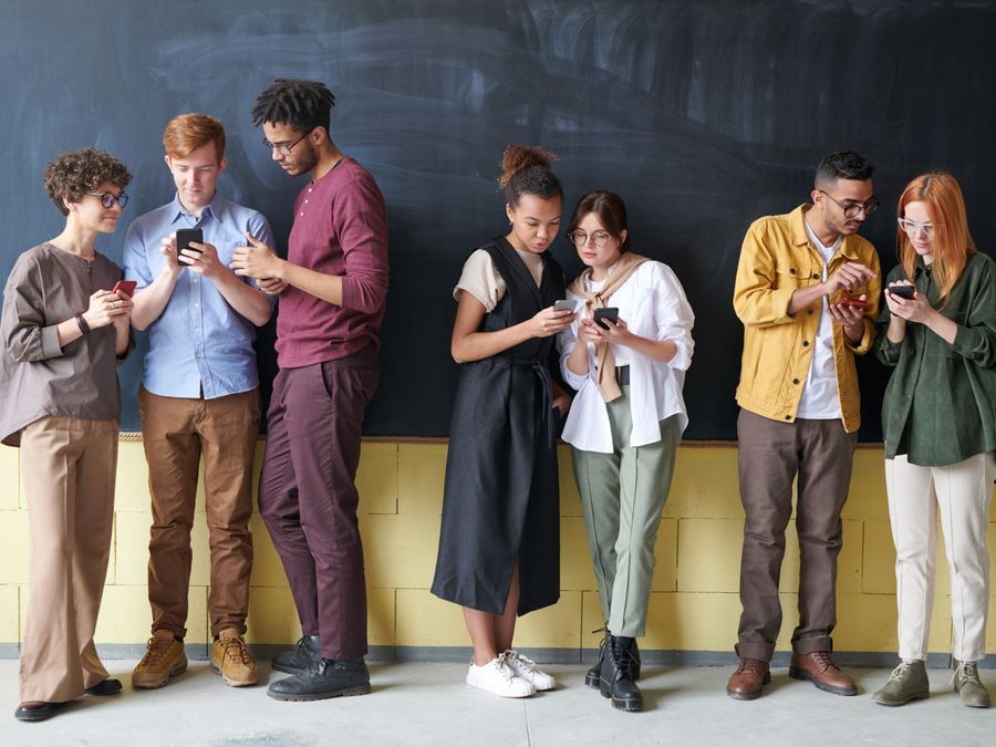 Young diverse adults using smartphones while standing against a blackboard, showcasing technology and connection.