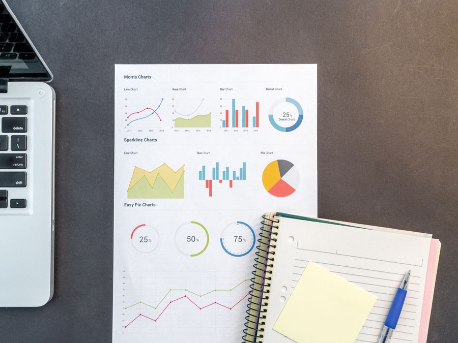 Top-down view of a desk with charts, a laptop, and notebooks, ideal for data analysis themes.
