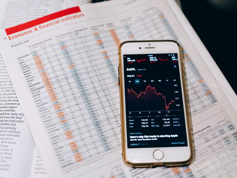 Smartphone displaying stock market data on papers with financial charts.