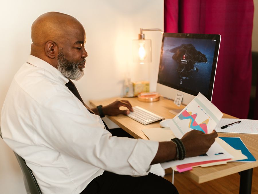 A mature professional working on business charts at a desk with a computer in an office setting.