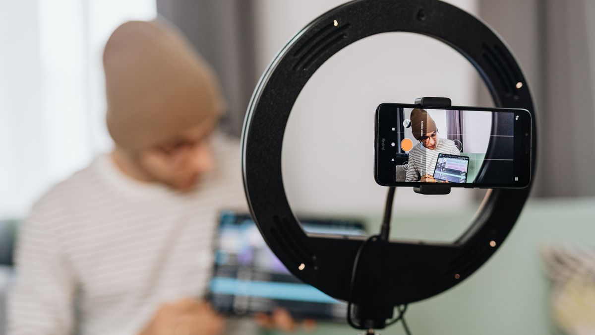 Man vlogging with a smartphone and ring light, focused on content creation indoors.