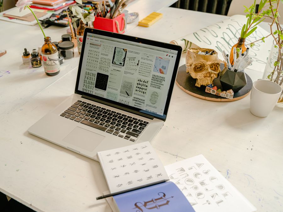 A creative workspace featuring a laptop, calligraphy book, and writing materials on a table.