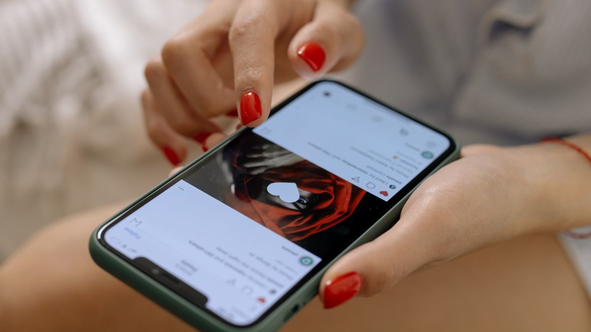 Close-up of a woman with red nails using a smartphone indoors, showcasing social media browsing.