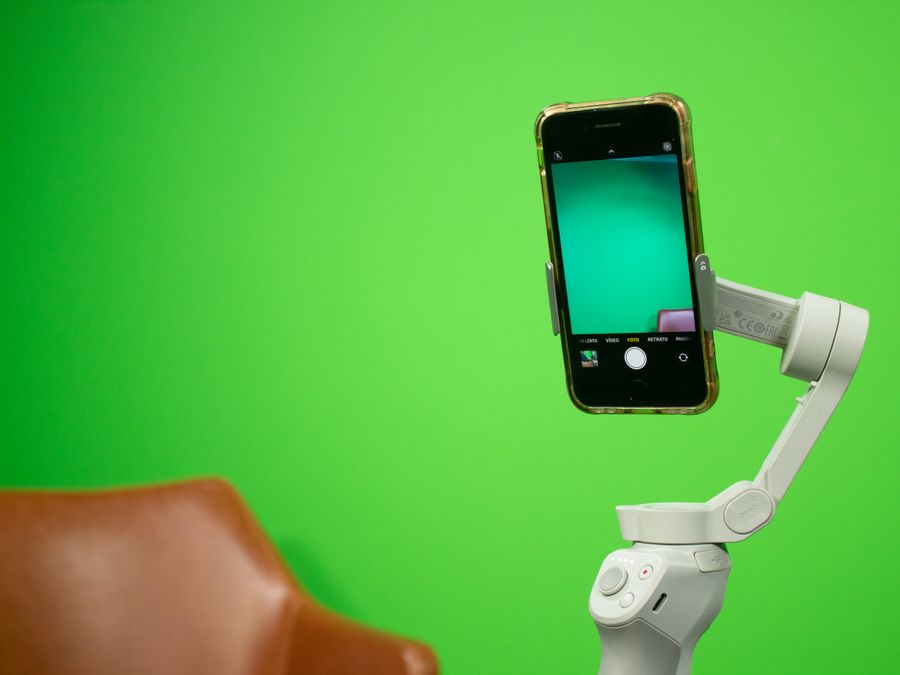 Smartphone mounted on a stabilizer in front of a green screen setup for video production.