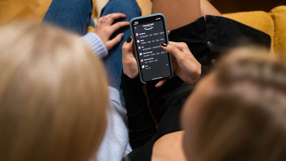 Two women browsing social media together on a smartphone indoors.