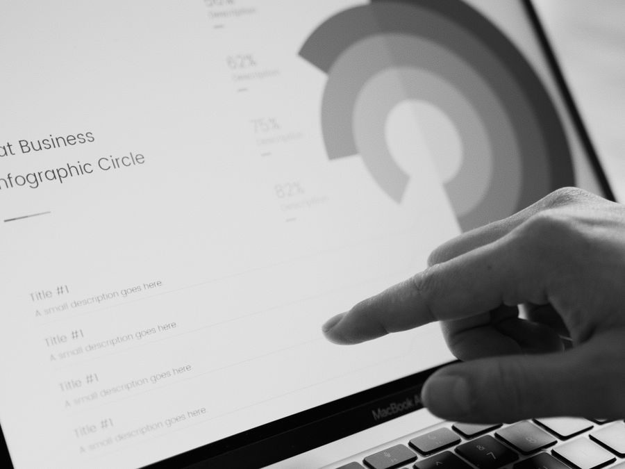Finger pointing at a business infographic circle on a laptop screen in grayscale.