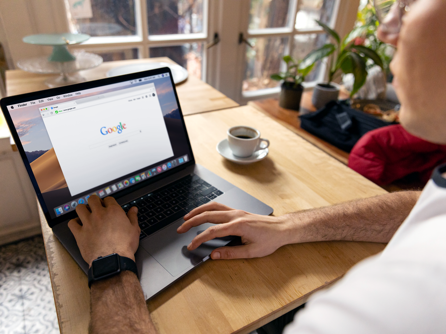 A person uses a laptop for internet browsing. A bright indoor setting with coffee on a wooden table.