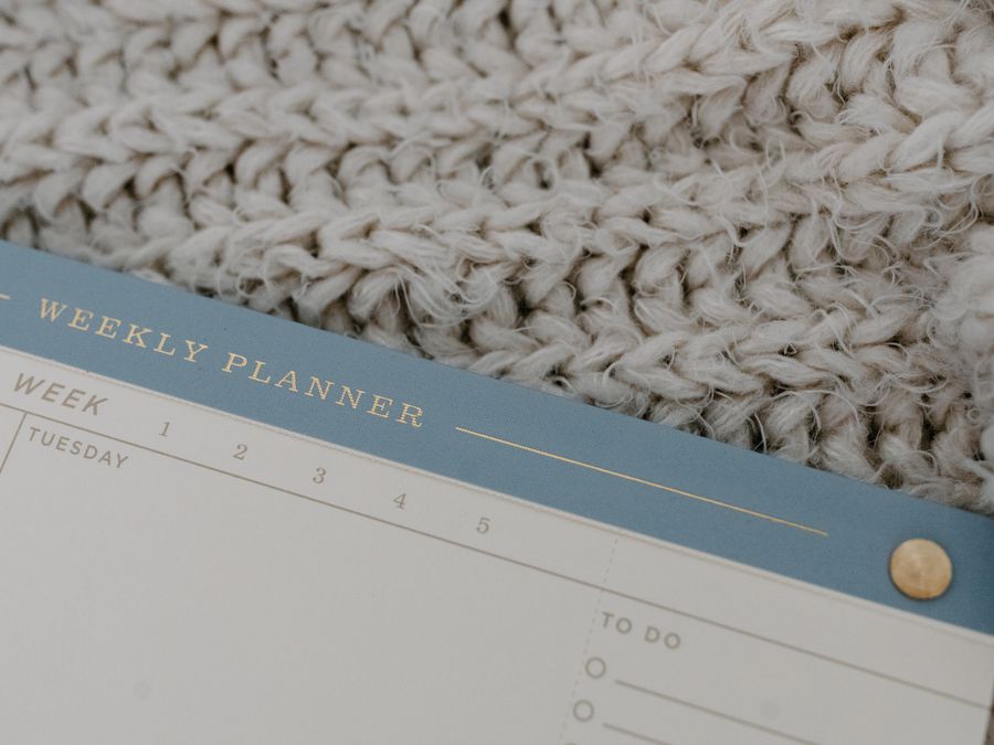 A weekly planner rests on a knitted fabric, providing a cozy vibe for planning.